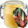 A close-up shot of a glass jar filled with a yellow substance, possibly honey or jam, with a lid featuring a print of tomatoes and cucumbers. Other empty glass jars are visible in the background. Produktbild-Vorschau