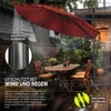 A patio umbrella is set up over a table and chairs on a wooden deck during a rain shower. Produktbild-Vorschau