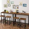 A bar set with a long table and four stools against a white wall with framed pictures and a shelf. Podgląd zdjęcia produktu