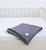A folded gray muslin blanket is placed on a white crib mattress, with the white bars of a crib visible in the background. Produktbild-Vorschau