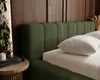 A close-up view of a green upholstered bed with pillows and a bedside table with books. Náhled obrázku produktu