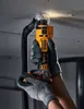 A person wearing gloves is using a DeWALT cordless drywall router to cut a circular hole in a ceiling, with a vacuum hose attached to collect dust. Podgląd zdjęcia produktu
