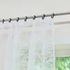A close-up view of white sheer curtains with a leaf pattern hanging from a metal curtain rod. Produktbild-Vorschau