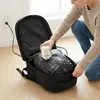 A person is using a small white vacuum pump to compress items inside an open black backpack. Produktbild-Vorschau