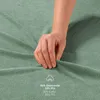 A hand is touching a green fabric, likely a bedsheet, with text and a cotton icon in the bottom right corner. Anteprima dell’immagine prodotto
