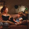A mother and daughter are reading books on a couch in a dimly lit room, with a floor lamp providing light. Produktbild-Vorschau