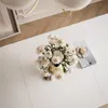A top-down view of a white table with a vase of white flowers and a cup of coffee on a book. Náhľad obrázku produktu