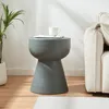 A dark gray concrete side table with a white mug and a book on top, placed next to a cream-colored sofa in a living room. Anteprima dell’immagine prodotto
