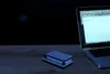 A laptop and a small electronic device are placed on a wooden surface in front of a dark background. Produktbild-Vorschau