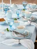 A table setting with blue tableware, including cups, saucers, a teapot, and a pitcher, arranged on a light blue tablecloth. Produktbild-Vorschau