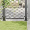 A close-up view of a metal fence post base with grass in the foreground and a chain-link fence in the background. Produktbild-Vorschau