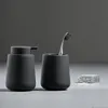 A minimalist bathroom set including a soap dispenser, toothbrush holder with a toothbrush, and a bar of soap on a gray surface against a dark gray background. Produktbild-Vorschau