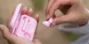 A person is holding pink earbuds and their charging case. Produktbild-Vorschau