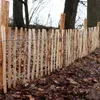 A wooden picket fence with wire supports in a natural outdoor setting with fallen leaves on the ground. Produktbild-Vorschau