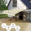 A beige awning is extended over a patio area next to a house, with lounge chairs on the deck. Anteprima dell’immagine prodotto