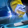 A welder is shown using a welding torch on a metal object, with a bundle of welding rods in the foreground. Produktbild-Vorschau
