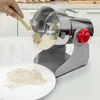 A hand is using a brush to clean a grain grinder that is dispensing flour onto a plate. Produktbild-Vorschau