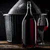 A bottle of red wine and a wine glass are placed on a wooden surface in front of a large wicker-covered demijohn. Anteprima dell’immagine prodotto
