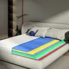 A cutaway view of a mattress showing its layered construction, placed on a bed in a bedroom setting. Produktbild-Vorschau