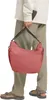 A person wearing casual clothing and sandals is holding a red shoulder bag. Produktbild-Vorschau
