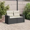 A dark gray rattan two-seater sofa with beige cushions sits on a brick patio, surrounded by greenery and string lights. Produktbild-Vorschau