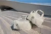 Two light-colored duffel bags are placed on concrete steps in front of a modern building. Voir les images du produit