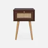 A dark wood bedside table with a rattan drawer front and wooden legs, presented against a white background. Produktbild-Vorschau