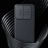 A black phone case with a textured pattern and a camera cover is shown against a black background with swirling metallic ribbons. Náhľad obrázku produktu