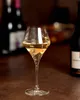 A glass of white wine on a wooden surface, with bottles in the background. Produktbild-Vorschau