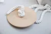 A wooden disc with a thick white rope tied to it, lying on a light gray surface. Podgląd zdjęcia produktu