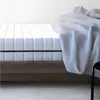 A close-up view of a mattress on a bed frame, with a blanket draped over it. Produktbild-Vorschau