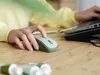 A person's hands are using a wireless mouse on a wooden desk, with a laptop in the background. Produktbild-Vorschau