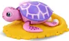 A pink toy turtle with a purple shell sits on a yellow sandy base. Produktbild-Vorschau
