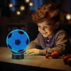 A young boy is looking at a glowing soccer ball lamp on a table. Produktbild-Vorschau