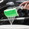 A hand holding a car wash brush with green sponge and soap suds, dripping water into a white bucket. Produktbild-Vorschau