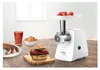 A Bosch meat grinder is shown on a wooden table with food items like sausages, a burger, juice, and coleslaw. Anteprima dell’immagine prodotto