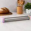A stainless steel rolling pin with colorful spacer rings is placed on a marble countertop, with a loaf of bread and kitchen utensils in the background. Produktbild-Vorschau