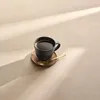 A cup of coffee on a saucer with a spoon, with light casting shadows. Produktbild-Vorschau