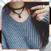 A close-up shot of a person wearing a grey knitted sweater and a black choker necklace with a rectangular pendant. Produktbild-Vorschau