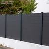 A dark gray fence made of horizontal planks supported by vertical posts, set against a background of green trees and a white building. Produktbild-Vorschau