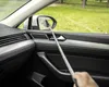 A person is holding a selfie stick with a phone attached, aiming it at a car's side mirror. The car is parked outdoors with grass and trees visible in the background. Anteprima dell’immagine prodotto