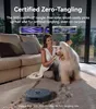 A woman is petting a dog on a carpeted floor, with a robot vacuum cleaner nearby. The image highlights the tangle-free roller brush feature of the robot vacuum. Anteprima dell’immagine prodotto