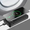 A black power bank is charging a smartphone, with a view of an airplane window in the background. Produktbild-Vorschau