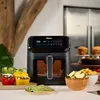 An air fryer is shown on a kitchen counter with prepared food around it. Produktbild-Vorschau