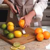 A person is zesting an orange with a Microplane grater over a cutting board with other citrus fruits. Anteprima dell’immagine prodotto