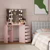 A bedroom scene featuring a pink vanity table with a lighted mirror and a bed with a gray headboard. Voir les images du produit
