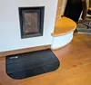 A black fire-resistant mat is placed on a wooden floor in front of a fireplace. Náhled obrázku produktu