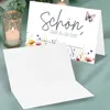 A greeting card with floral and butterfly design, placed next to a lit candle and an envelope. Produktbild-Vorschau