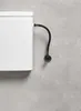 A close-up view of a white toilet tank with a black flexible hose connected to a water supply valve on a gray wall. Anteprima dell’immagine prodotto