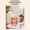 A soy milk maker is shown on a table in a living room setting, with a person in the background. Produktbild-Vorschau